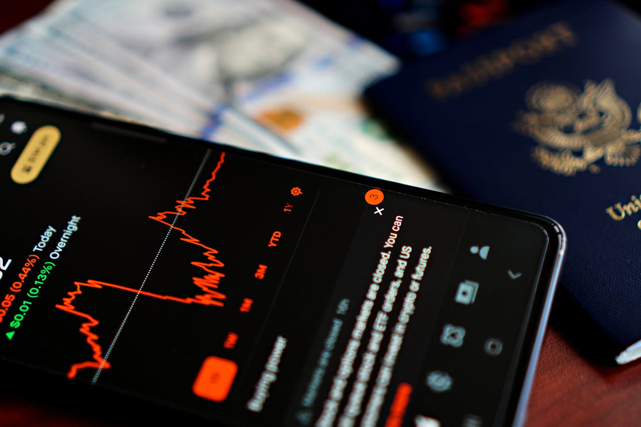 journey Close-up of a smartphone displaying a stock market app alongside a US passport and currency.