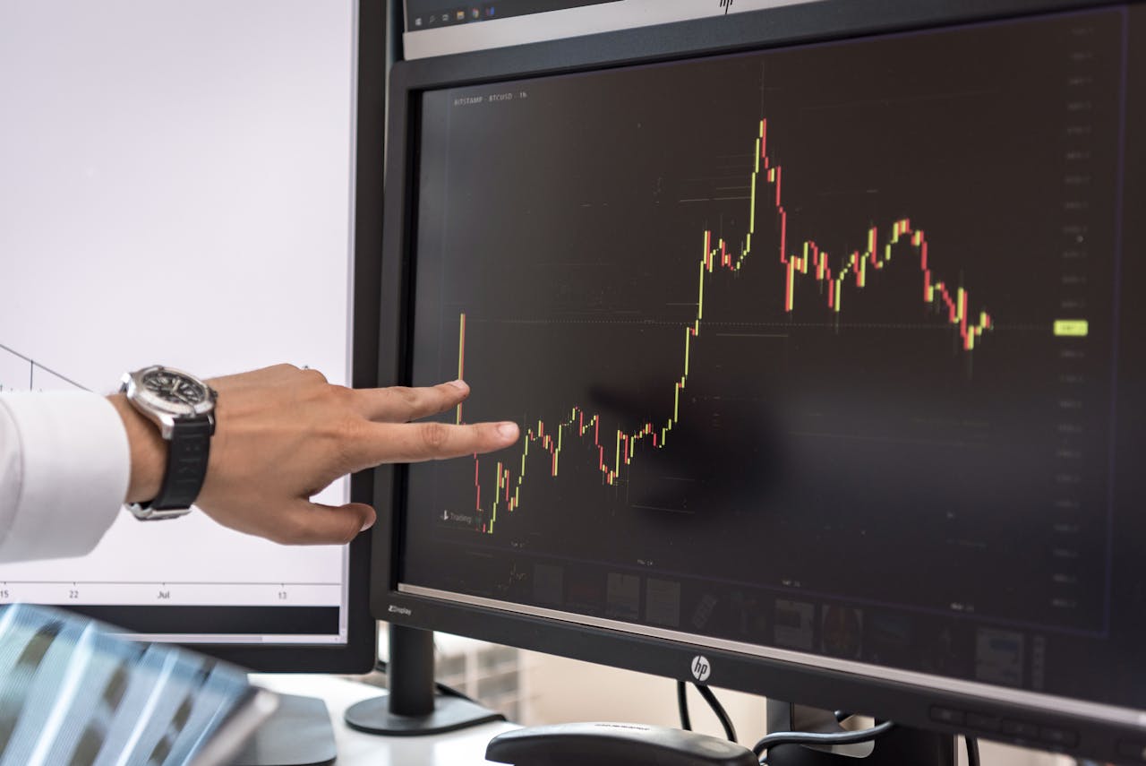 why-choose-us Detailed view of a hand pointing at a cryptocurrency trading graph on a monitor.